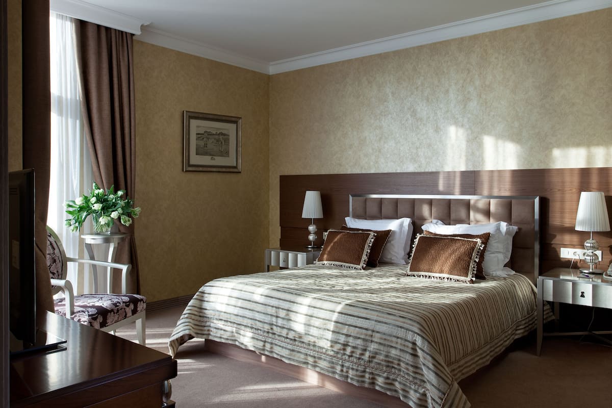 A hotel room with a large bed, two bedside tables, a chair, a desk, and a potted plant.