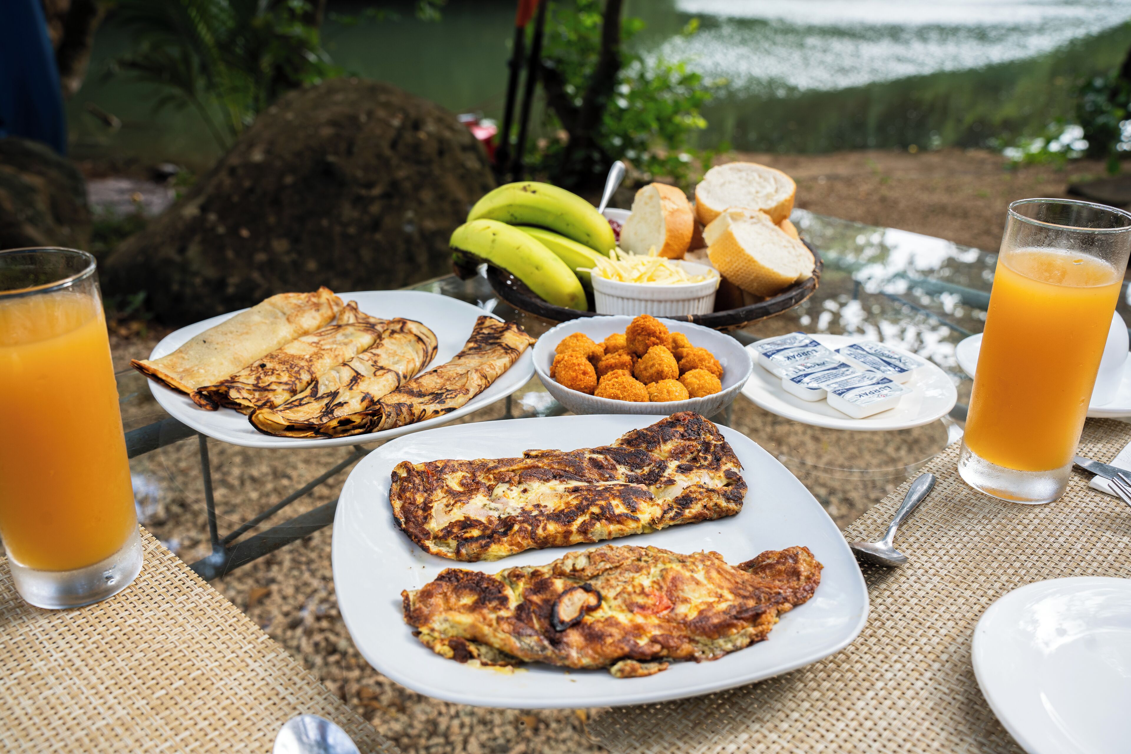 Una mesa de desayuno con platos de comida, incluyendo huevos, pan y plátanos, y vasos de jugo de naranja.