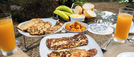 Una mesa de desayuno con platos de comida, incluyendo huevos, pan y plátanos, y vasos de jugo de naranja.