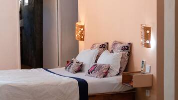 A neatly made bed with a white and blue bedspread, two pillows with floral patterns, and a wooden bedside table with a lamp.