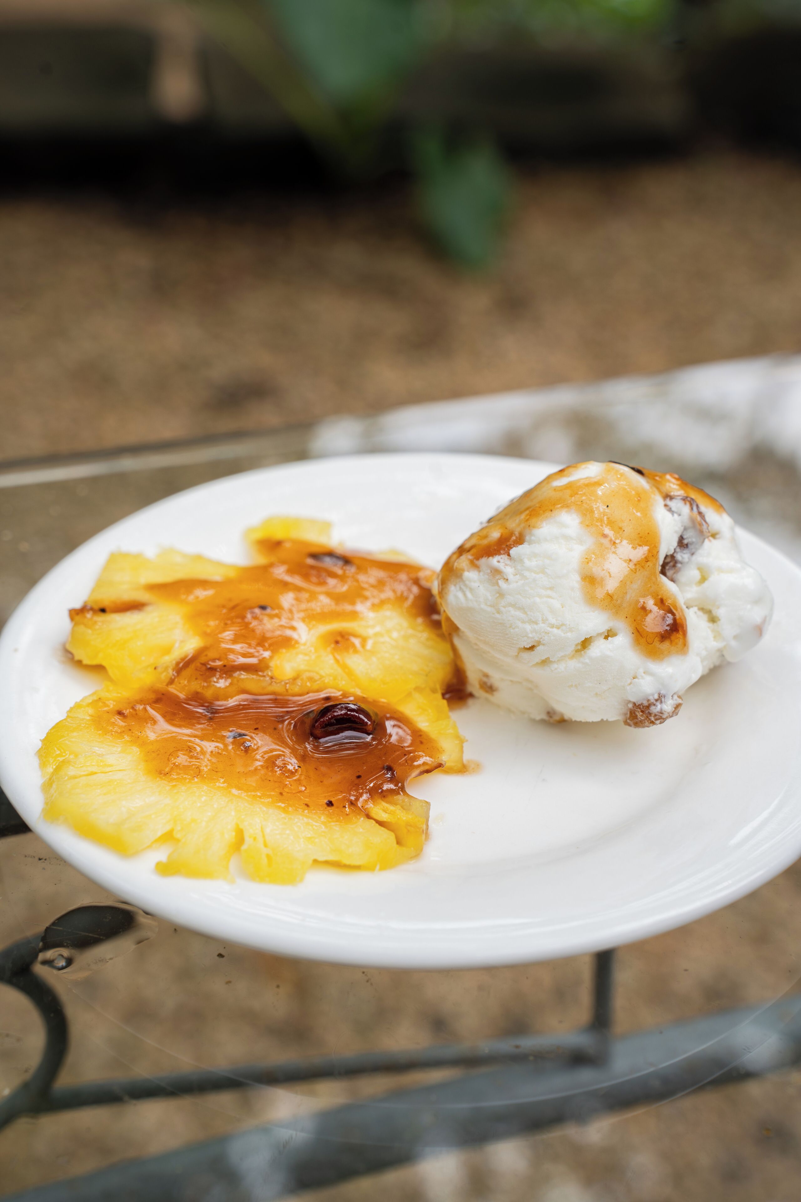 A plate with pineapple chunks and a scoop of vanilla ice cream on a white plate.