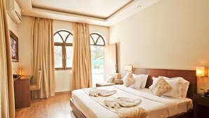 Habitación de hotel con una cama grande, dos mesitas de noche, un escritorio y una ventana con cortinas.