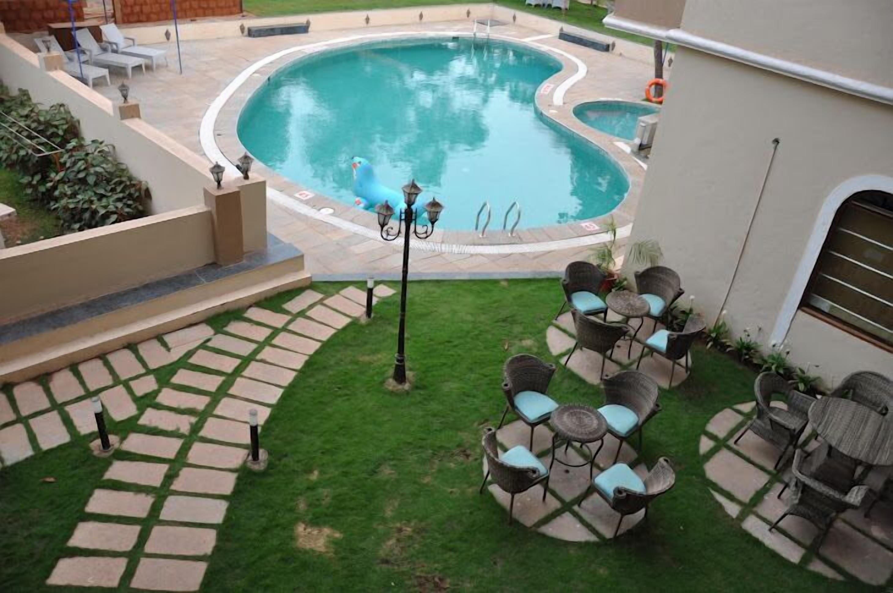 A swimming pool with a unique shape, surrounded by a paved patio with outdoor seating and a small lawn area.