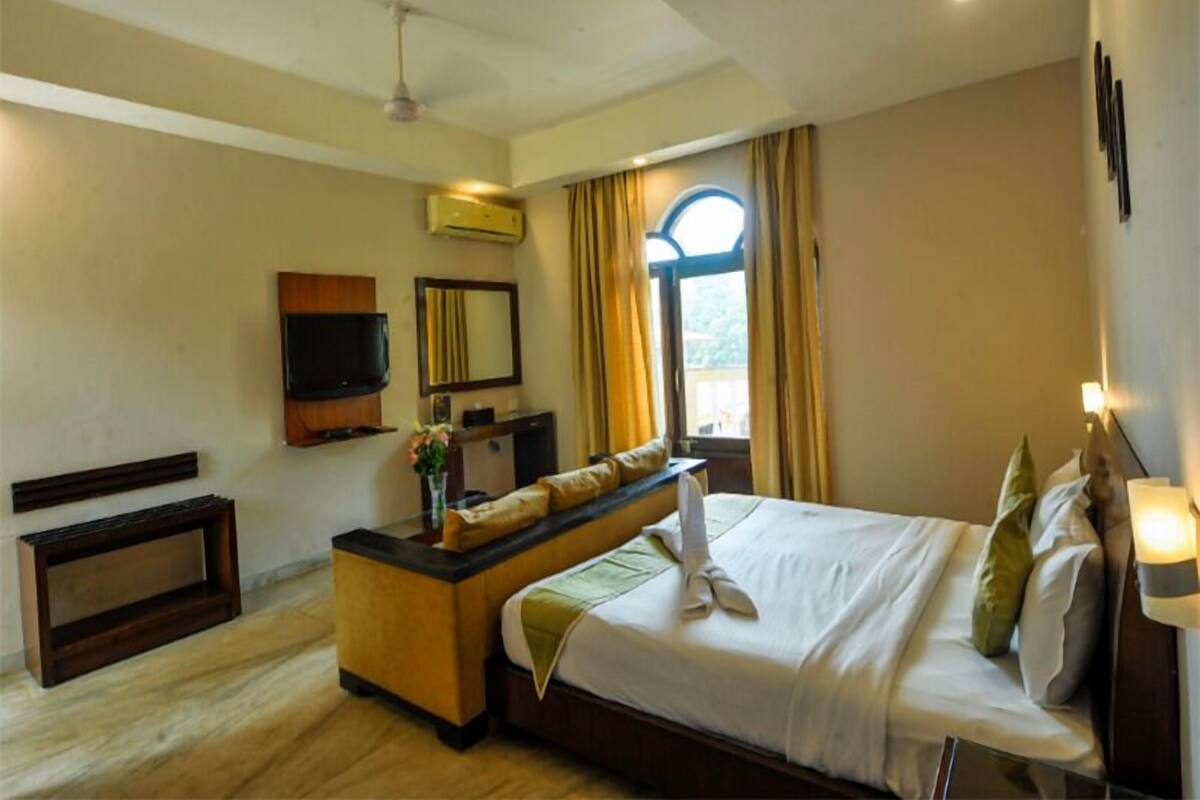 A hotel room with a bed, a desk, a television, and a window with curtains.