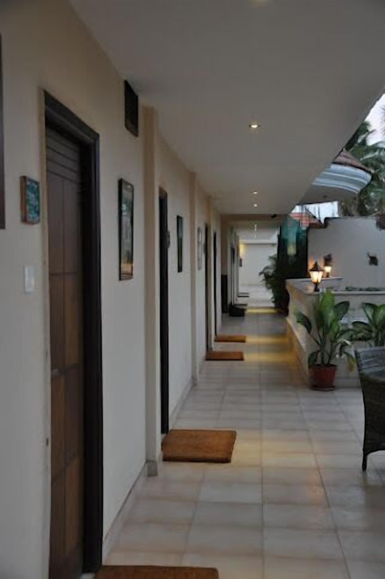 A corridor with doors on the left, a bench on the right, and a small table with a lamp.