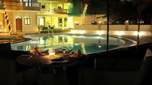 Un área junto a la piscina con una mesa preparada para comer, un jacuzzi y un edificio con balcones al fondo.