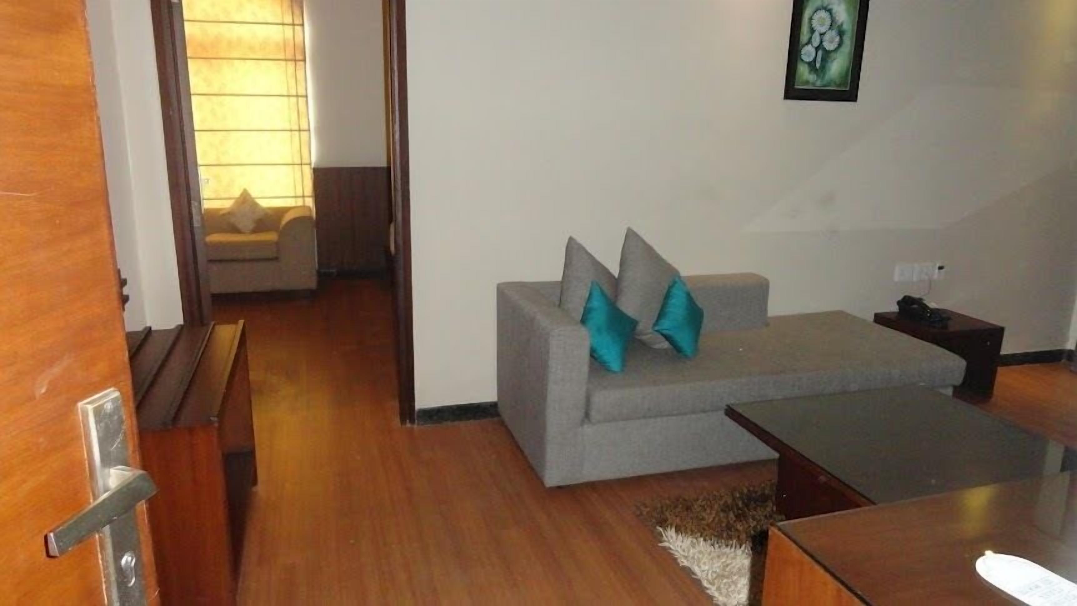 A living room with a grey sofa, two teal cushions, a wooden coffee table, and a framed artwork on the wall.