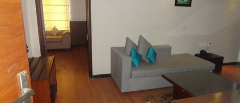 A living room with a grey sofa, two teal cushions, a wooden coffee table, and a framed artwork on the wall.