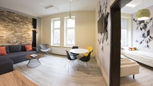 A modern living room with a stone accent wall, a sofa, a coffee table, and a dining area with chairs. - Yourplace Central Apartments (Kraków)
