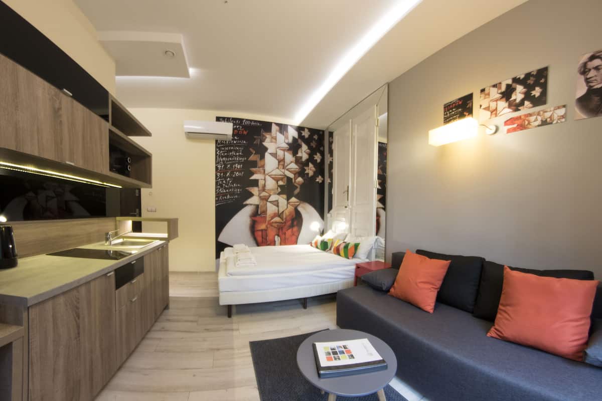 Una habitación de hotel moderna con kitchenette, una cama, un sofá y una pequeña mesa.