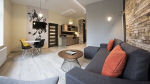 A modern living room with a grey sofa, orange cushions, a round coffee table, and a dining area with a white table and black chairs. - Yourplace Central Apartments (Kraków)
