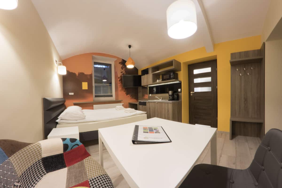 Una habitación de hotel moderna con cama, una pequeña mesa de comedor, un sofá, una zona de cocina y un armario.