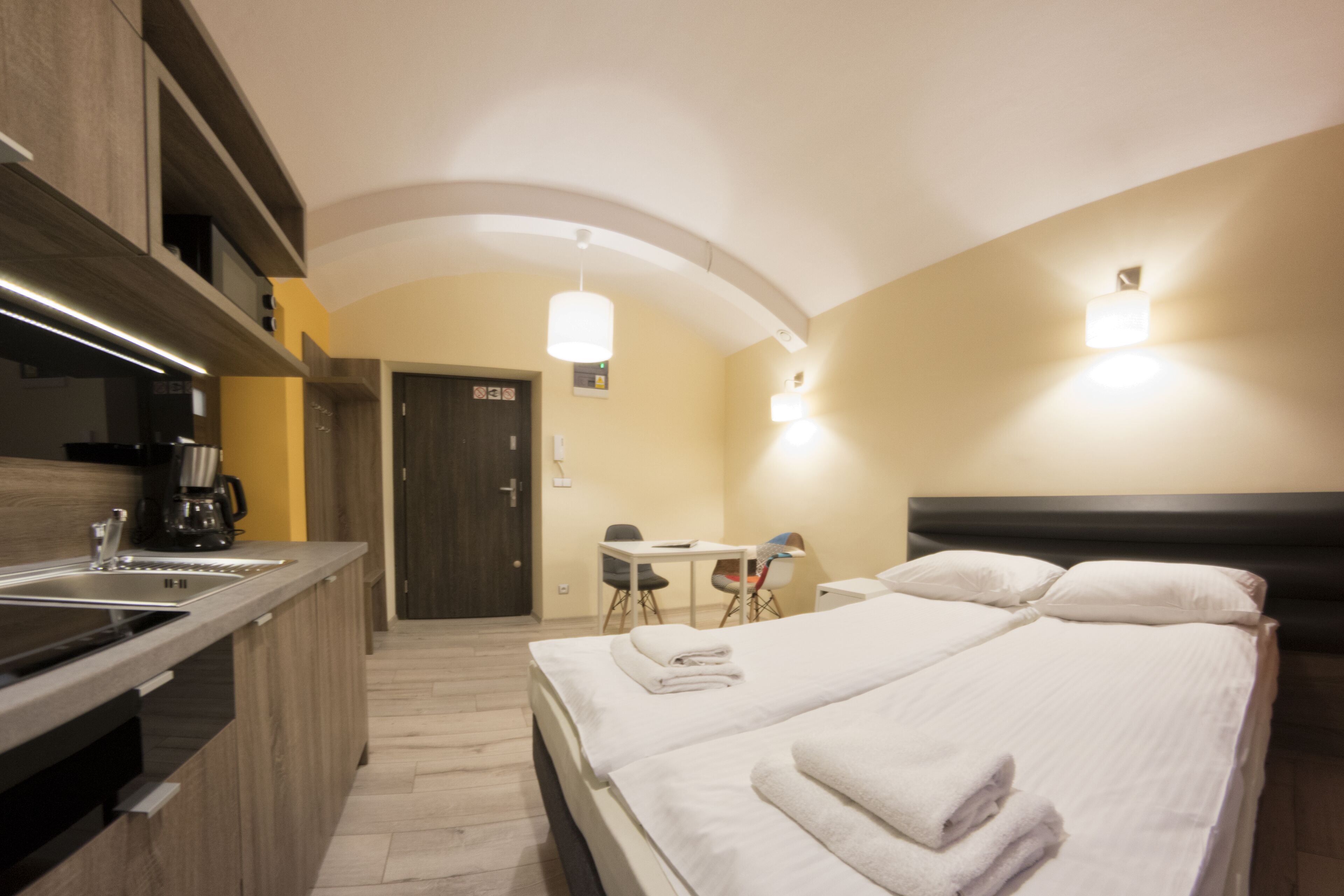 Habitación de hotel con kitchenette, una cama con ropa blanca, un escritorio y una silla.