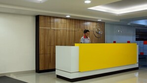 A reception desk with a wooden panel backdrop and a yellow counter. - Amaris Hotel Thamrin City - Jakarta (Jakarta)