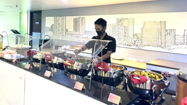 A buffet area with various food containers and a person serving food. - Amaris Hotel Thamrin City - Jakarta (Jakarta)