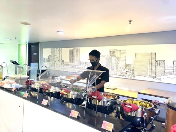 Un espace buffet avec différents récipients contenant de la nourriture et une personne qui sert les plats.