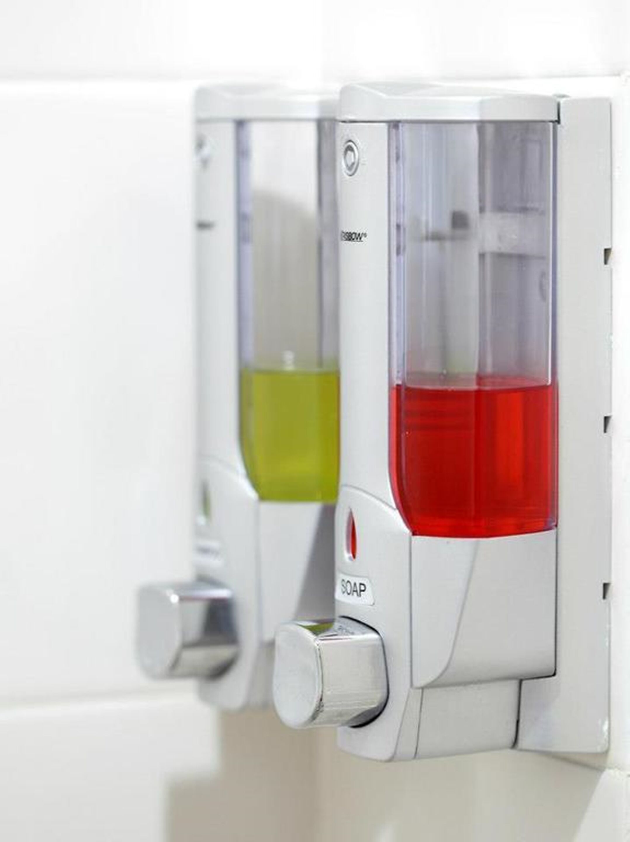 A wall-mounted soap dispenser with a clear container and a red liquid inside.
