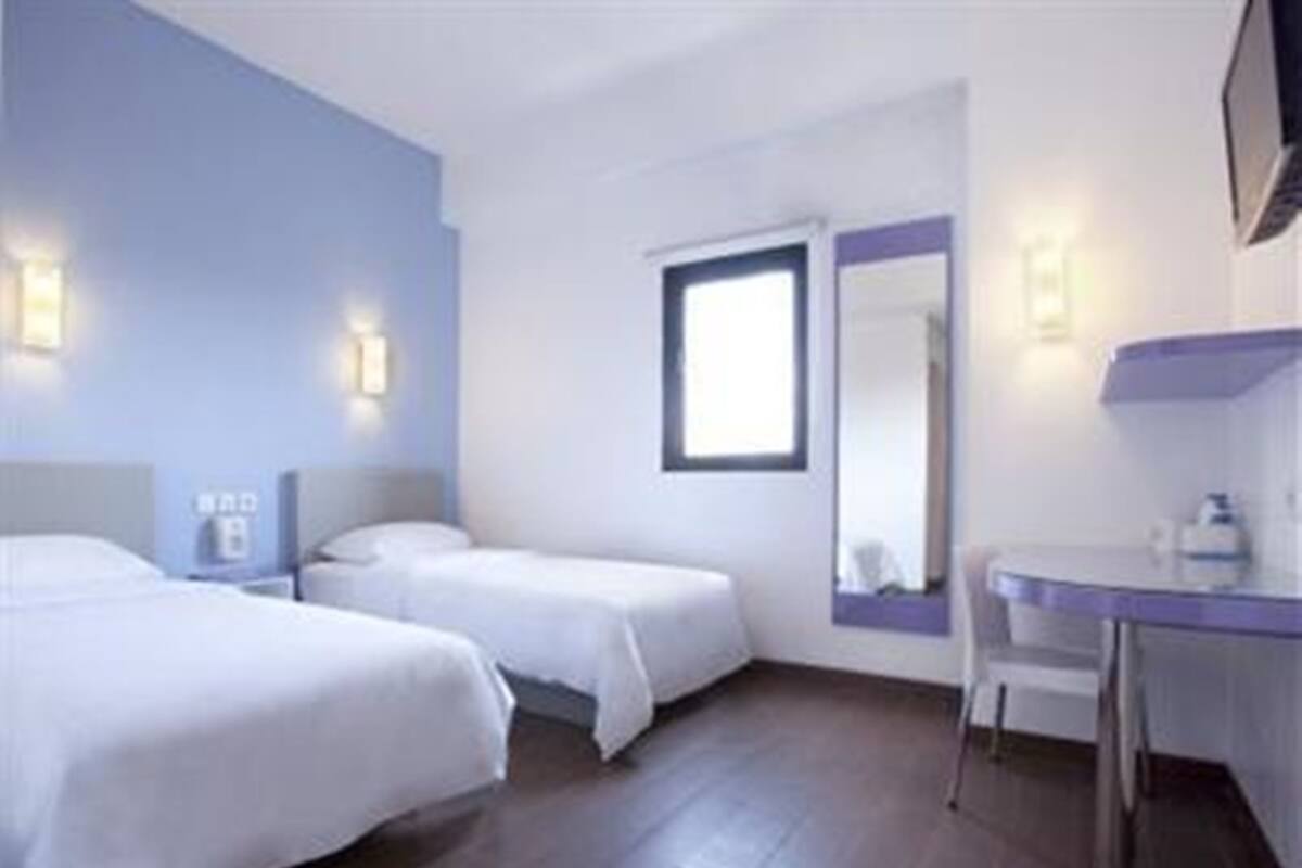 Ein Hotelzimmer mit zwei Betten, einem Schreibtisch, einem Stuhl, einem Spiegel und einem Fenster.