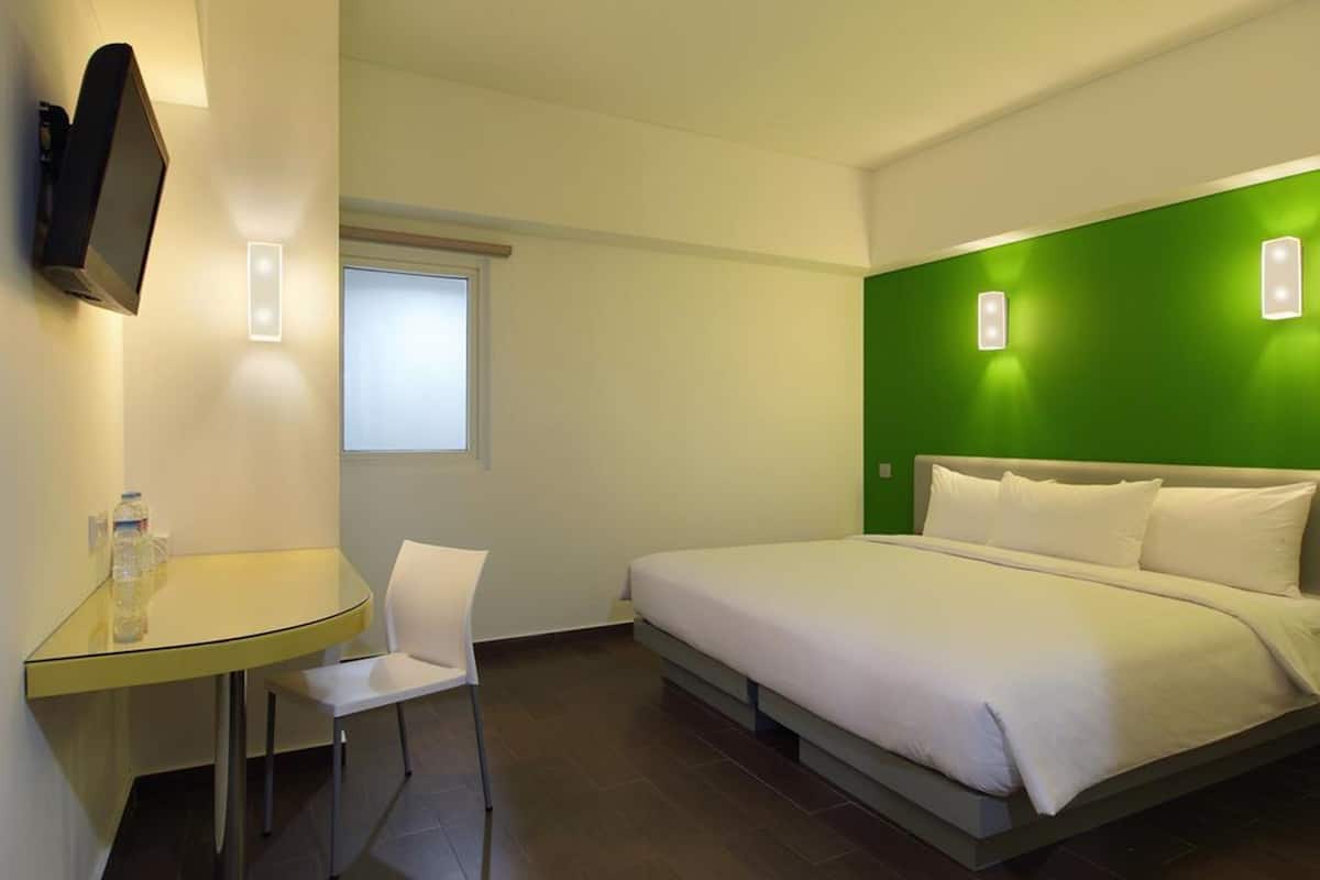 Ein Hotelzimmer mit Bett, einem kleinen Tisch mit Stuhl, einem an der Wand befestigten Fernseher und einem Fenster.