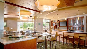 A modern hotel lobby with a central bar area, seating arrangements, and large windows providing natural light.