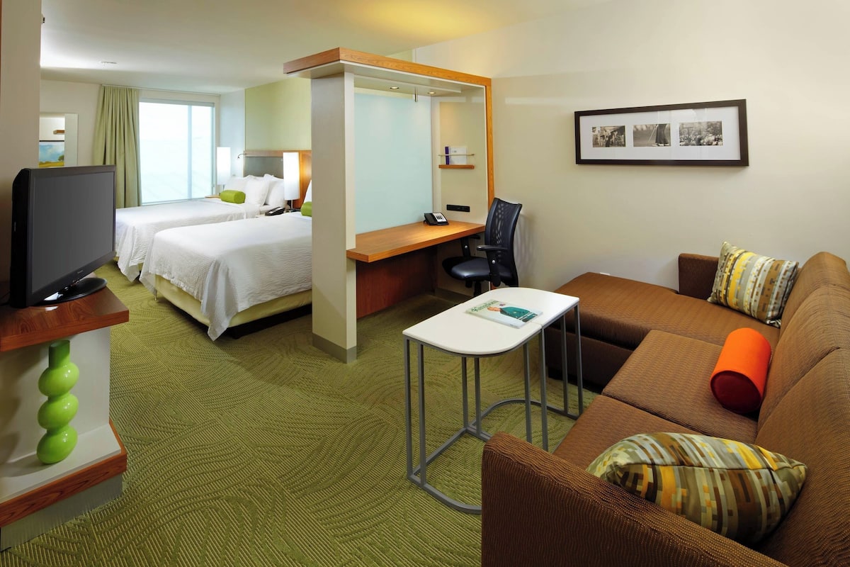 A hotel room with a bed, a desk, a TV, a couch, and a chair.