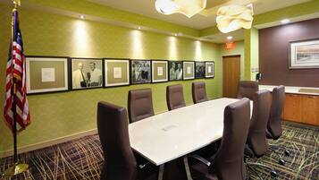 A conference room with a long table and six chairs, framed pictures on the wall, an American flag, and a reception desk.