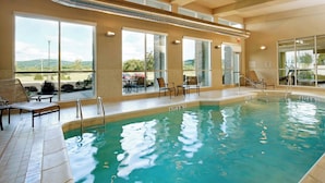 An indoor swimming pool with clear water, sunlit by large windows, and surrounded by lounge chairs.