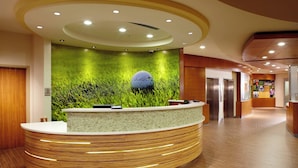 A reception area with a curved reception desk, a green wall with grass and a golf ball, and a wooden floor.