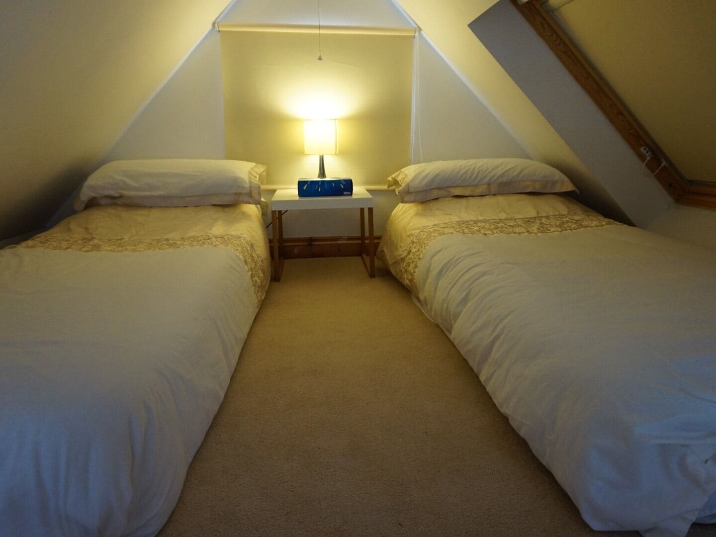Een kleine, knusse kamer met twee enkele bedden, een nachtkastje met een lamp en een schuine plafond.