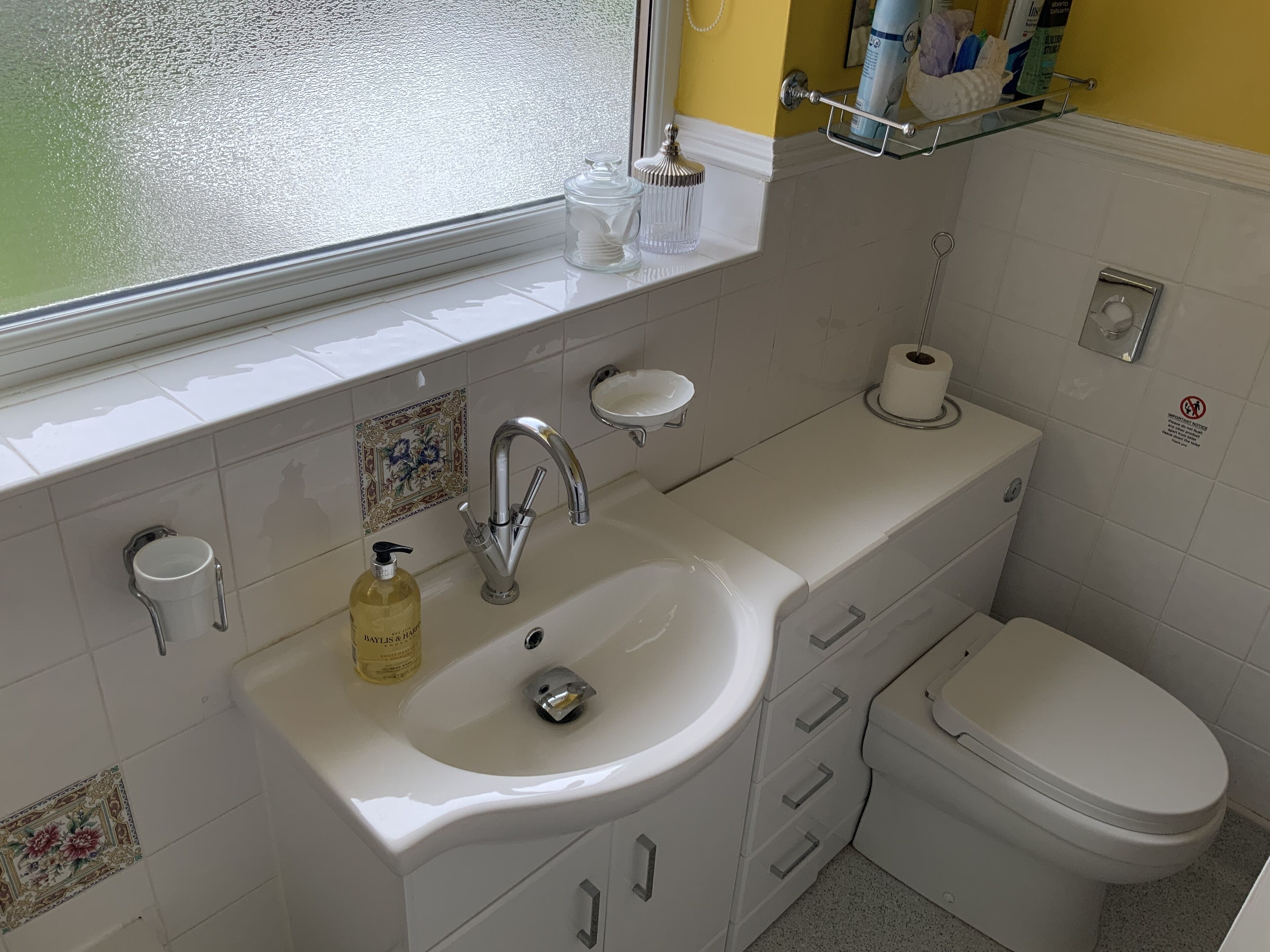 Une salle de bain avec un lavabo blanc, des toilettes et une fenêtre.