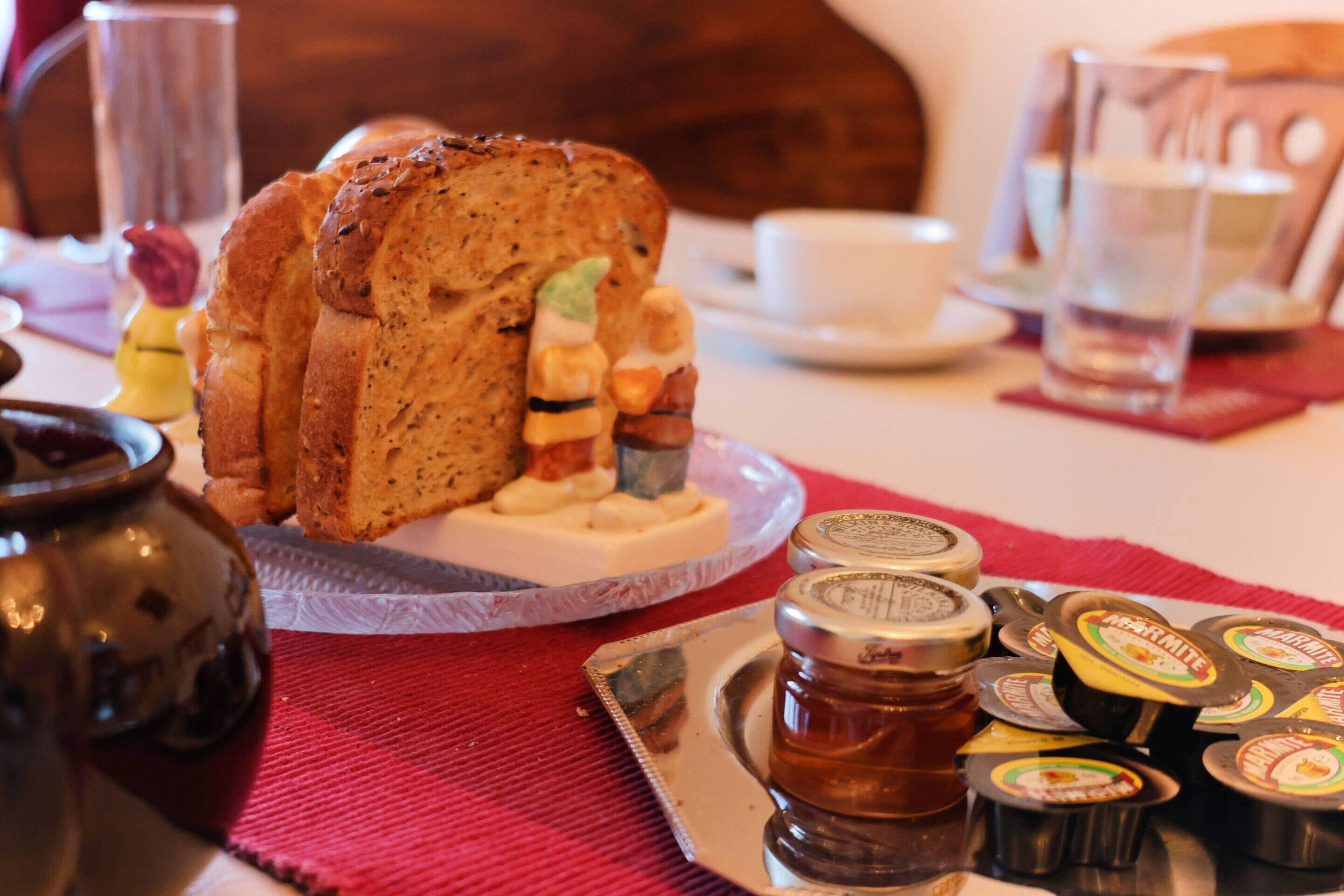 Una mesa con pan, mermeladas y una taza.