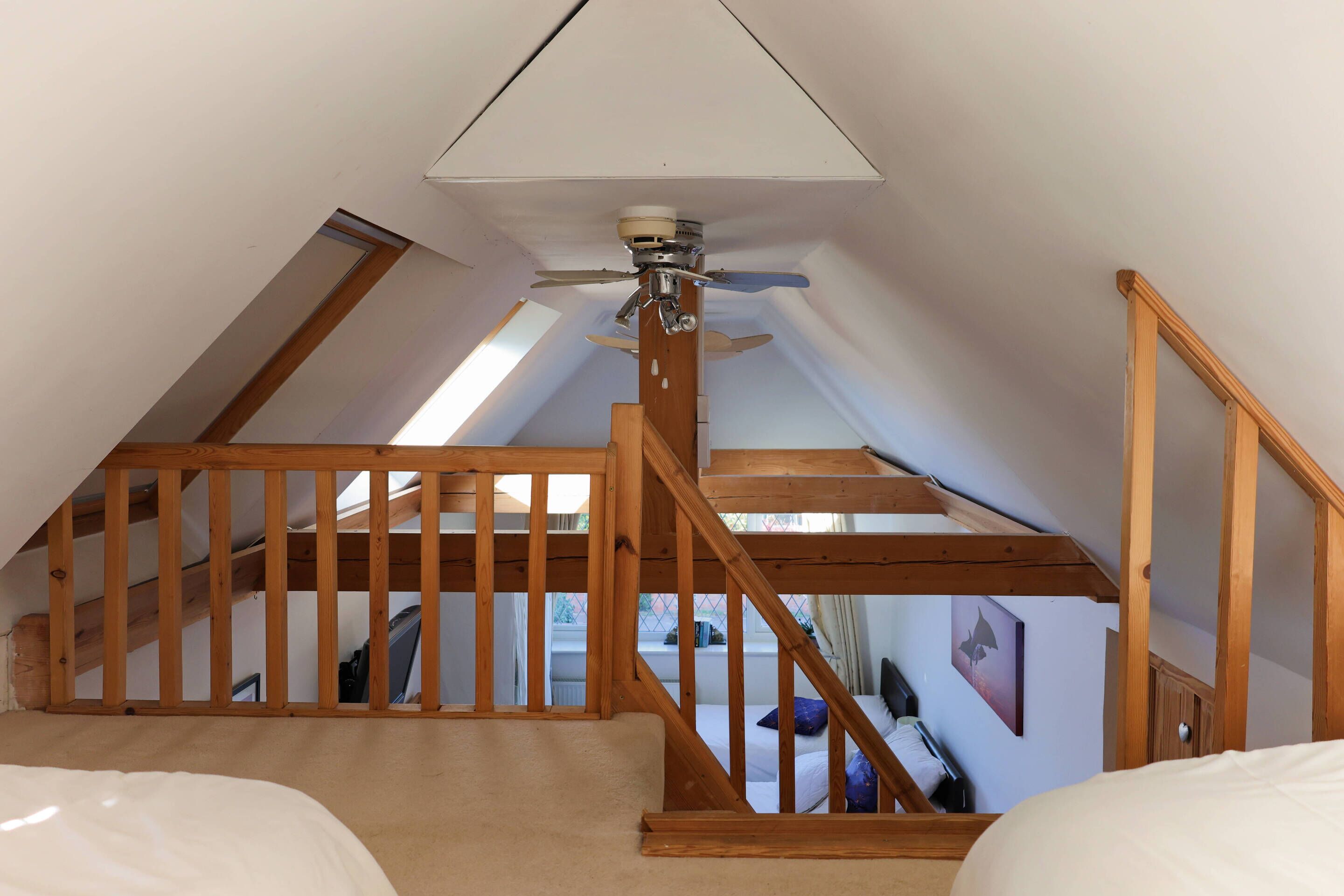 An attic bedroom with a sloped ceiling, wooden staircase, and a ceiling fan.