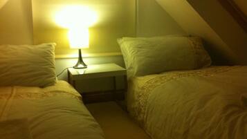 A small, dimly lit room with two beds and a nightstand.