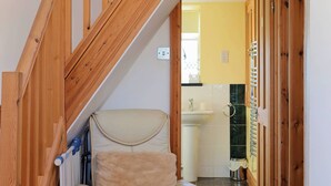 Una escalera de madera que lleva al segundo piso, un sillón color beige, un radiador y un baño con lavamanos y espejo.