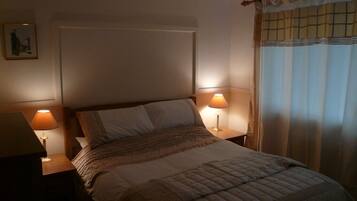 Un dormitorio con una cama, dos lámparas de noche, una mesita de noche y una ventana con cortinas.