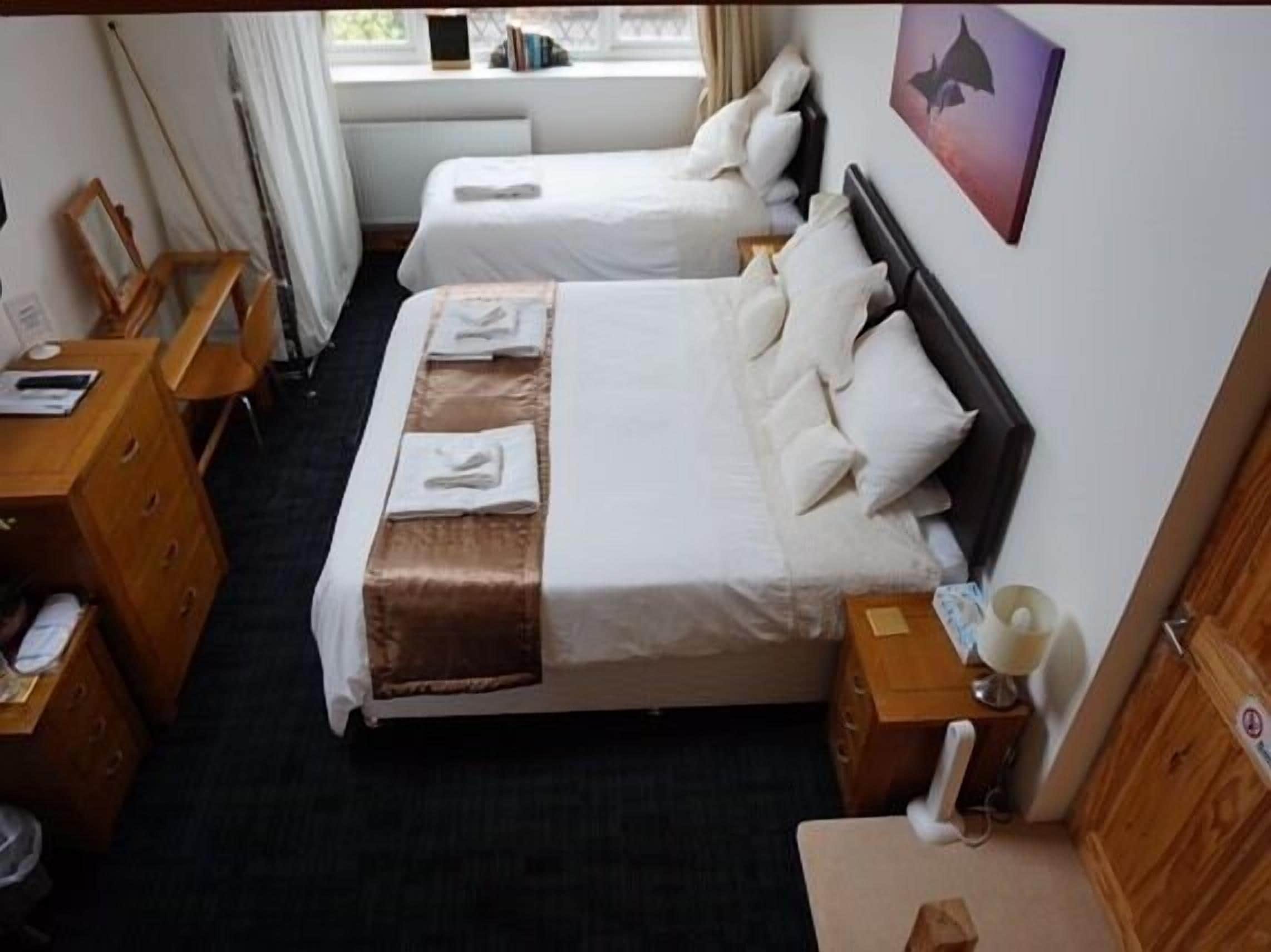 Een hotelkamer met twee enkele bedden, een houten dressoir, een bureau en een raam met gordijnen.