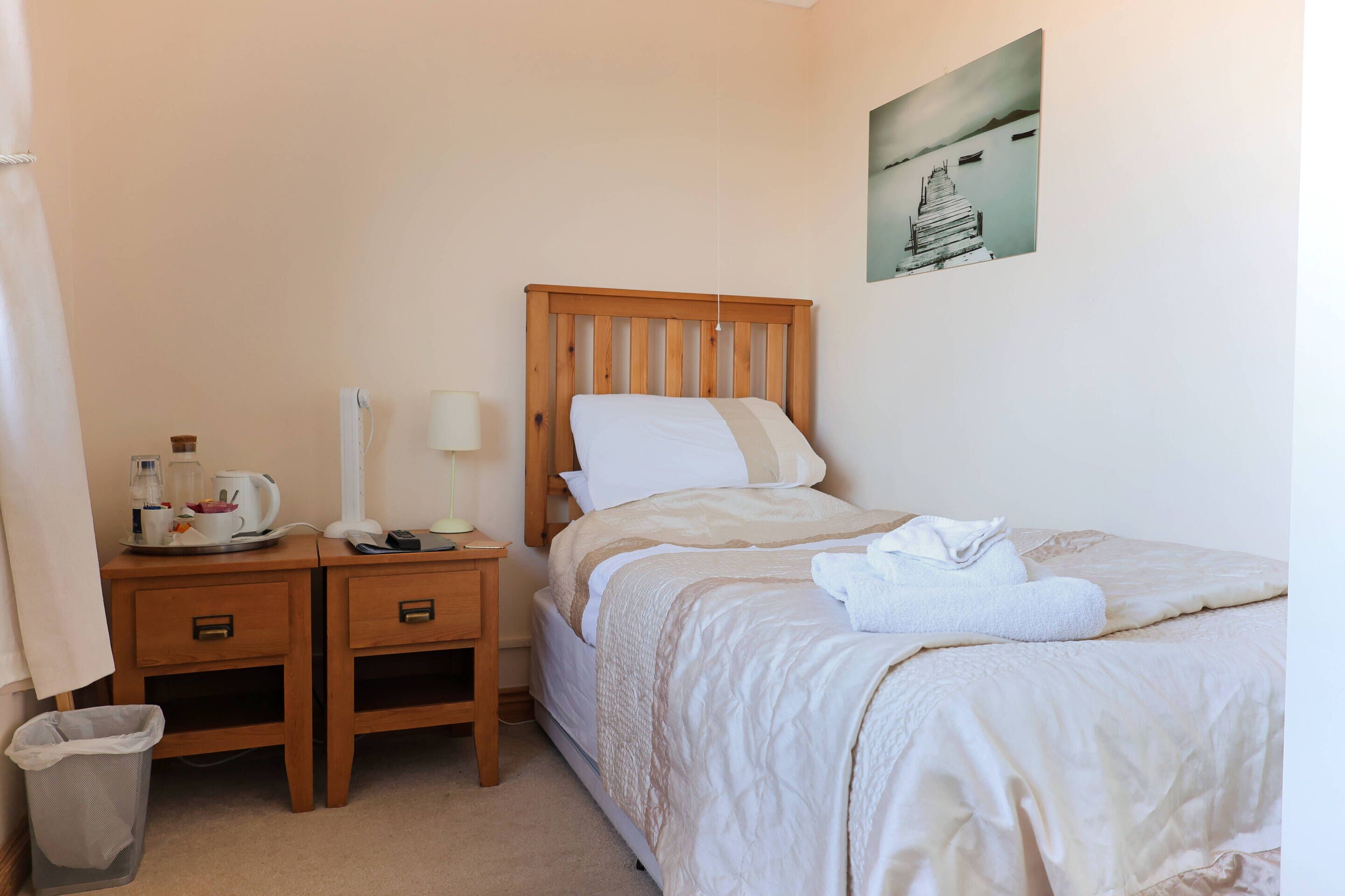 Une chambre d’hôtel bien rangée, avec un lit en bois, des tables de chevet, une poubelle et un tableau accroché au mur.