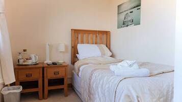 Une chambre d’hôtel bien rangée, avec un lit en bois, des tables de chevet, une poubelle et un tableau accroché au mur.