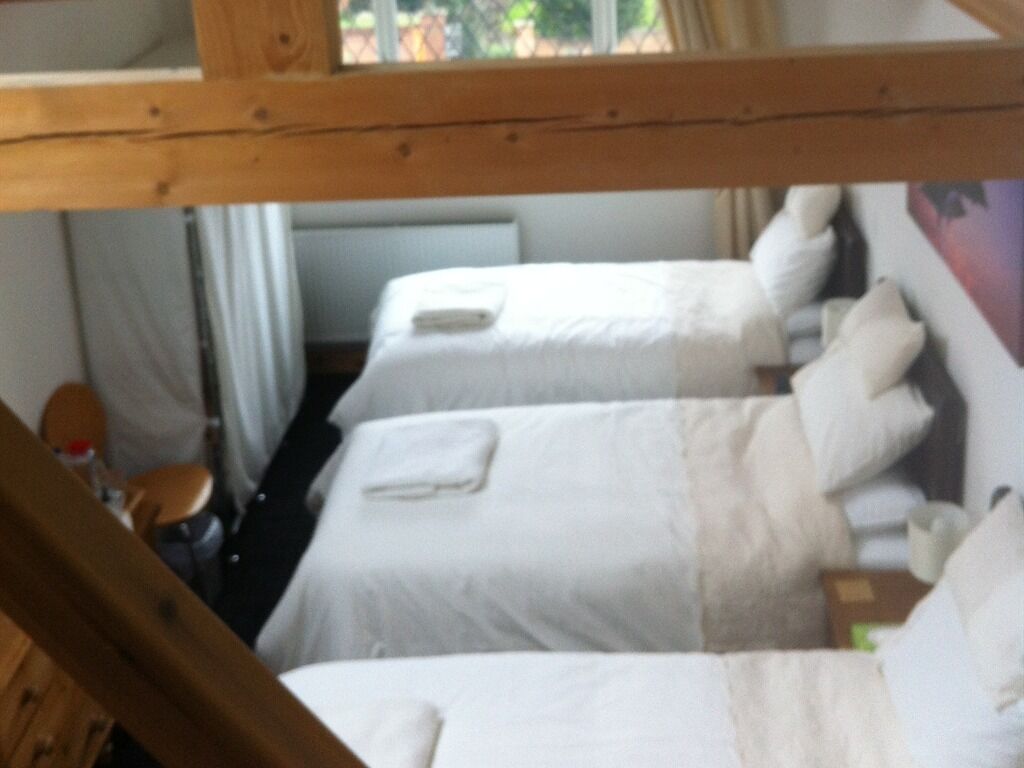 A room with two beds, each with white bedding and pillows, a wooden headboard, and a window with curtains.