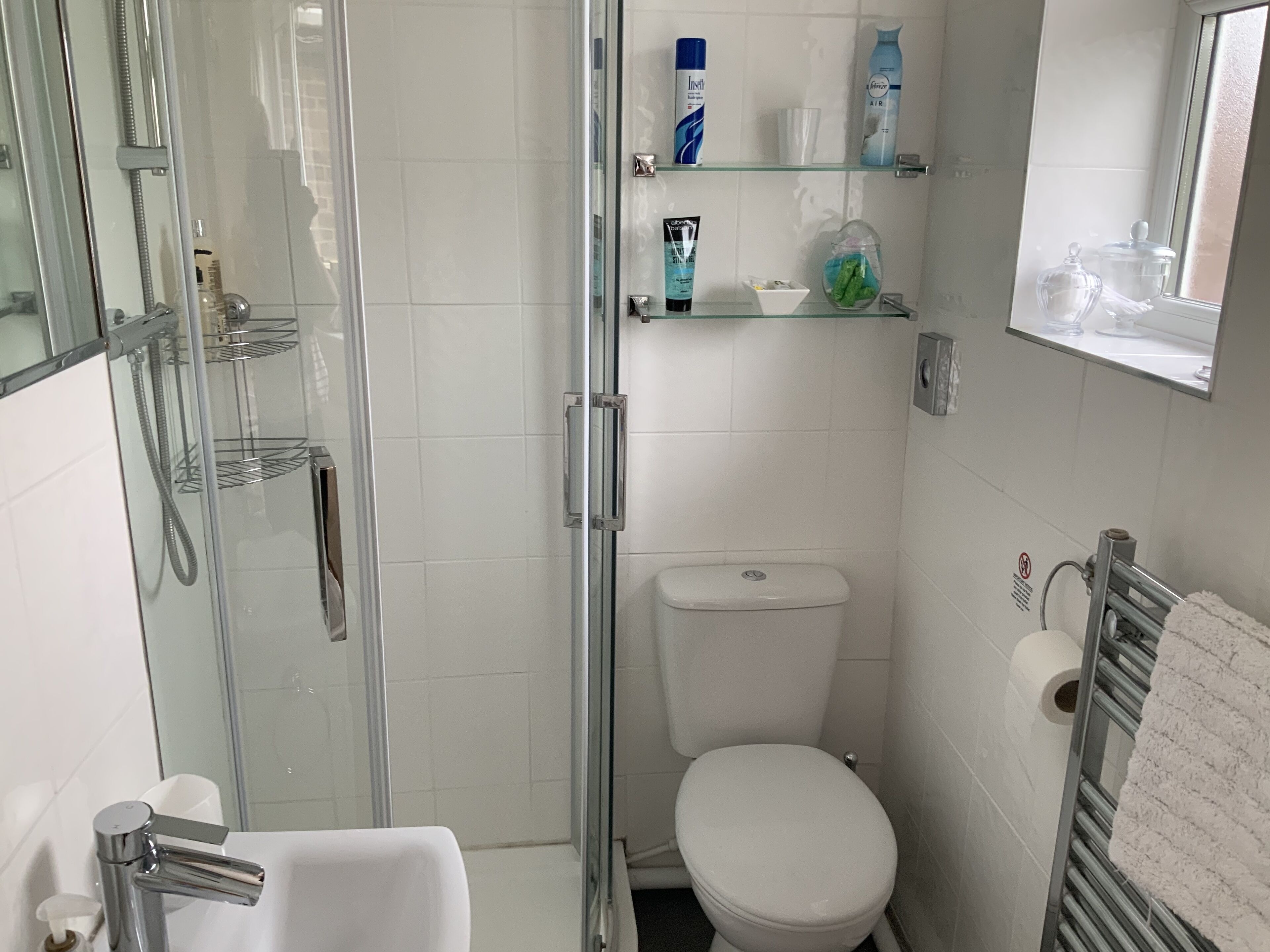 A modern bathroom with a glass-enclosed shower, a white toilet, and a glass shelf with toiletries.