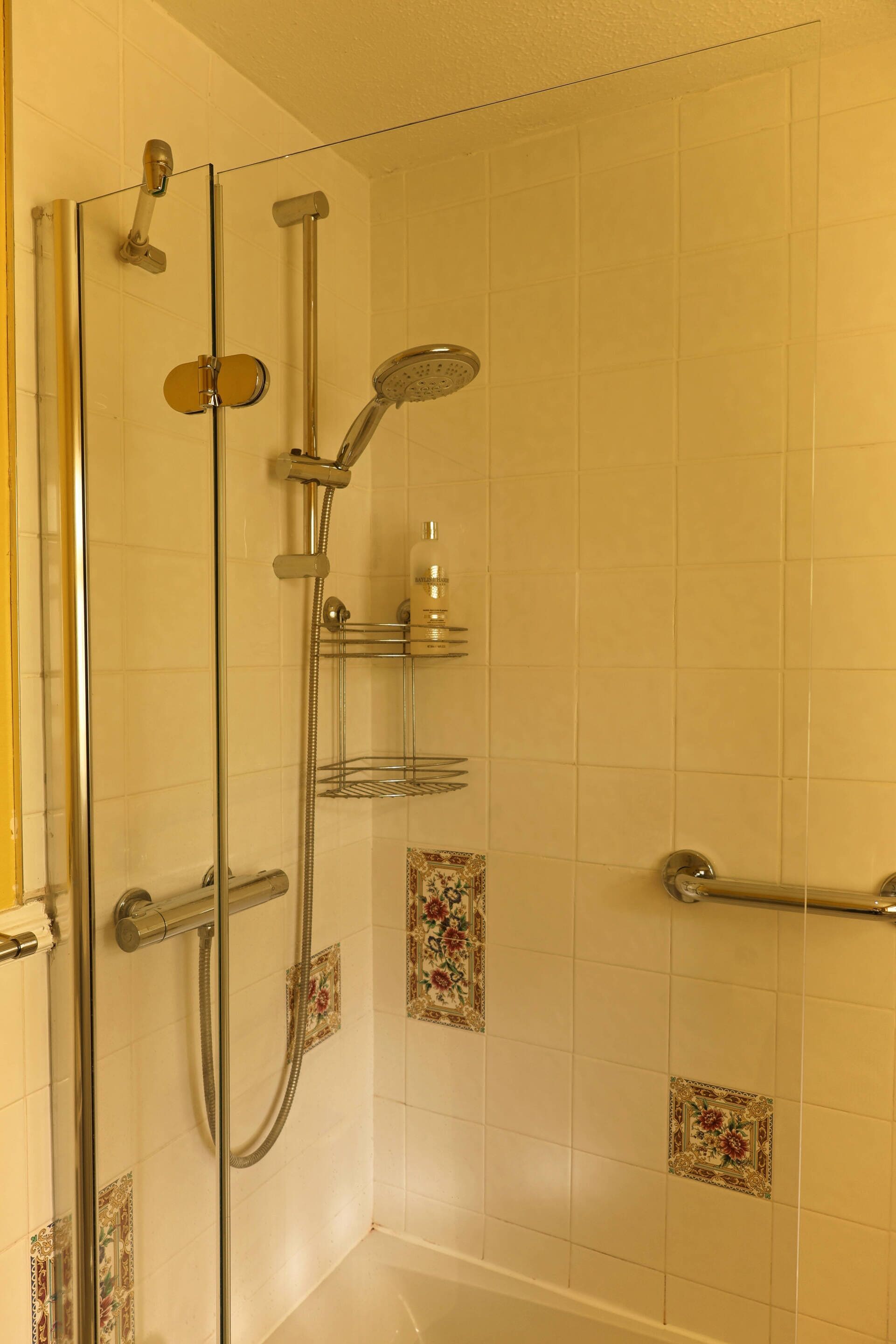 A glass-enclosed shower with a handheld showerhead and a wall-mounted faucet.