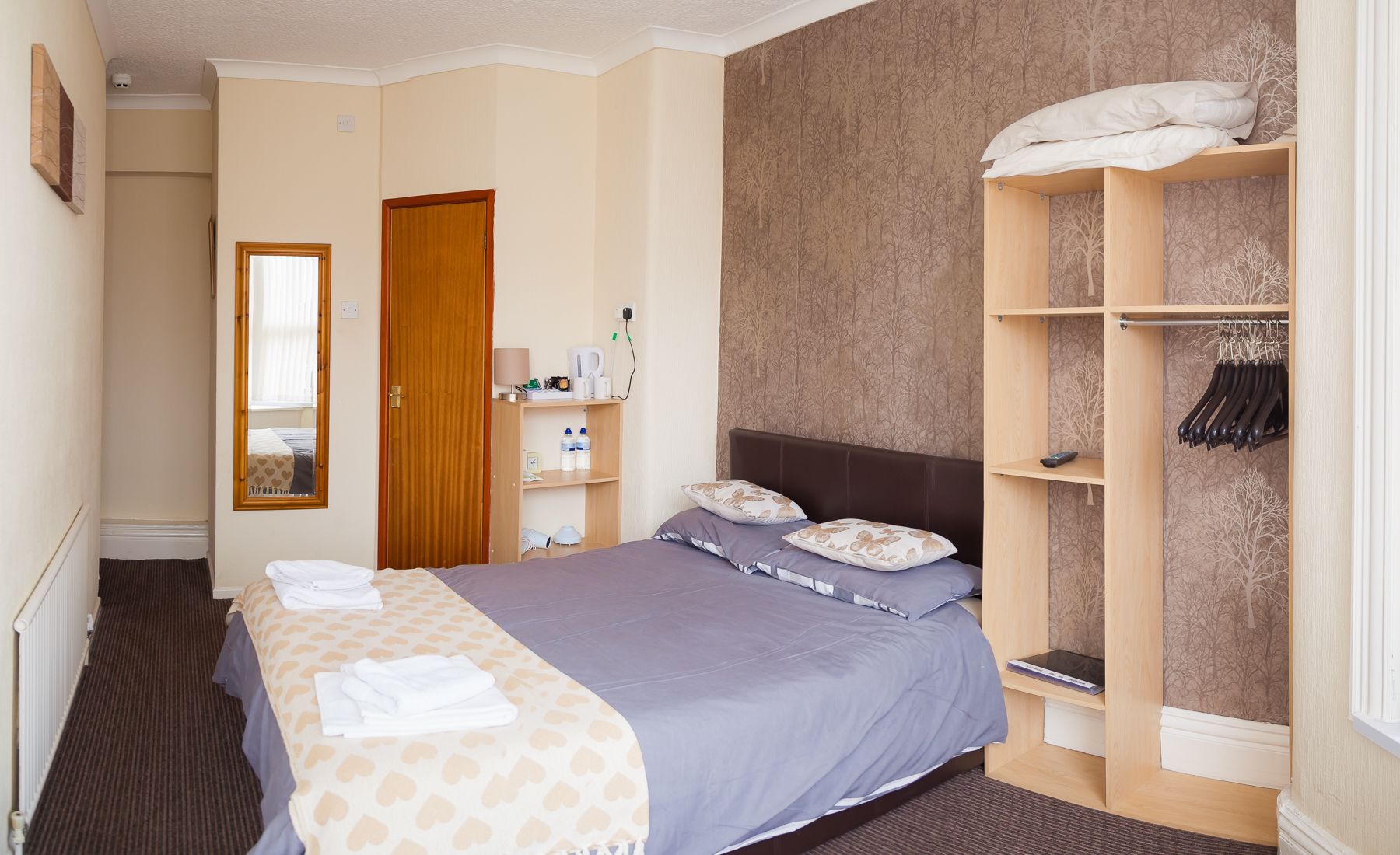 A hotel room with a bed, a wardrobe, a mirror, and a shelf with toiletries.