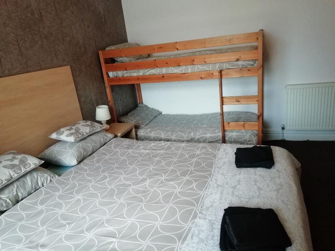 Een kamer met een stapelbed, een nachtkastje met een lamp en beddengoed met een patroon.