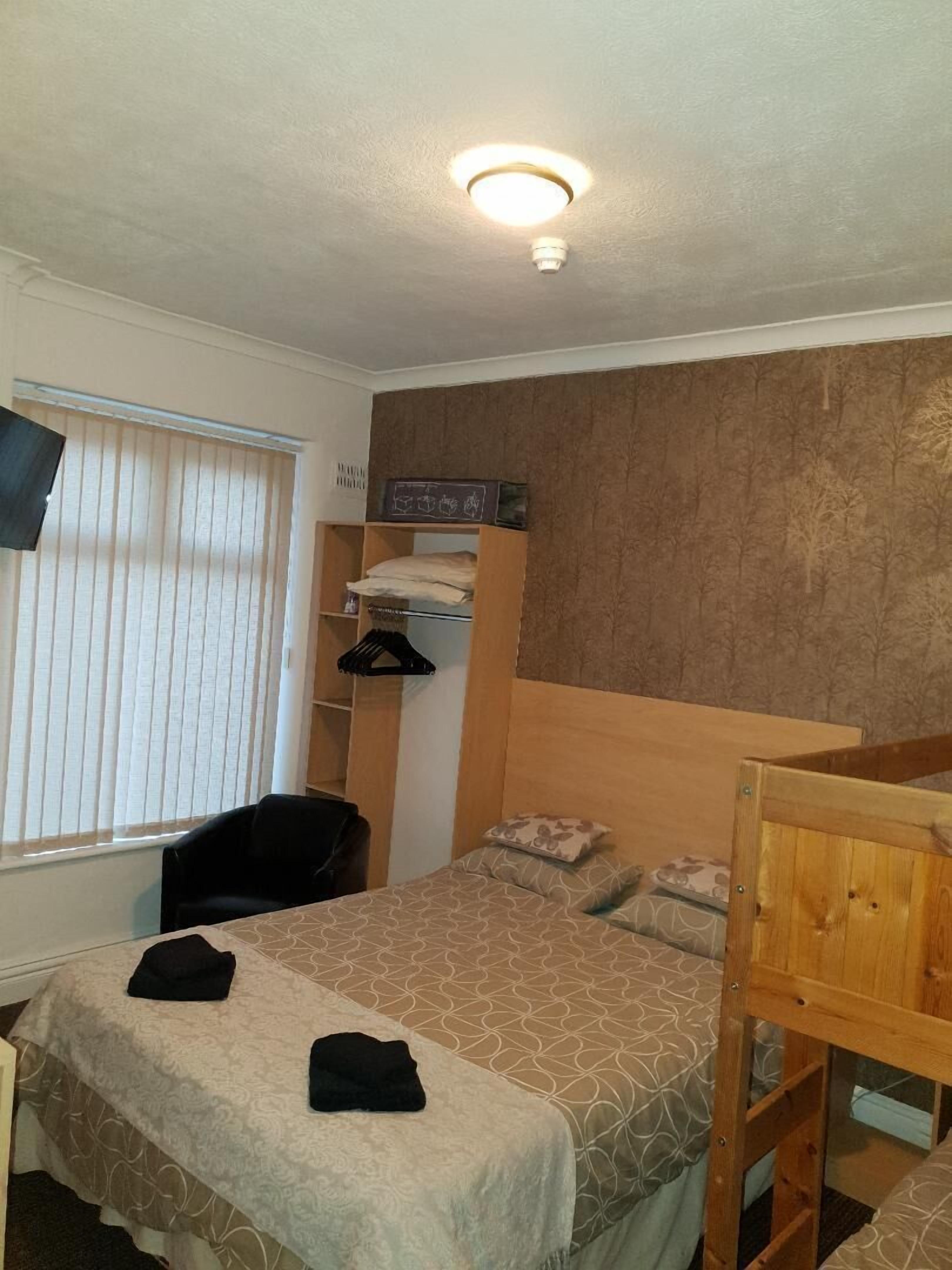 A dorm-style room with bunk beds, a desk, and a window with blinds.