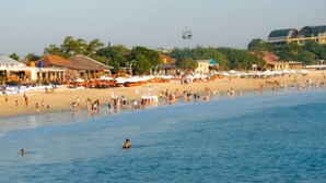 A beach with people swimming and sunbathing, umbrellas, and buildings in the background. - Villa Happy (Kedonganan)