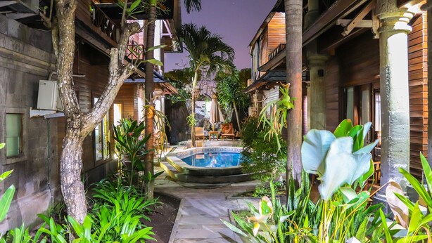 A courtyard with a pool, surrounded by wooden buildings and tropical plants. - Villa Happy (Kedonganan)