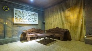 A room with a wooden sofa and a table, a wall with a relief sculpture, and a bamboo wall. - Villa Happy (Kedonganan)