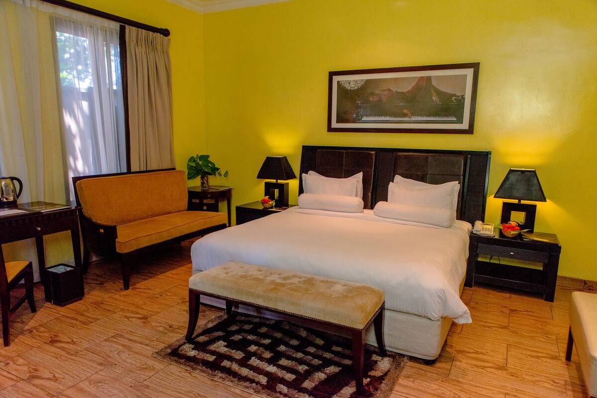 A hotel room with a large bed, a bench, a desk, and a chair. There are two bedside tables with lamps and a framed picture on the wall.