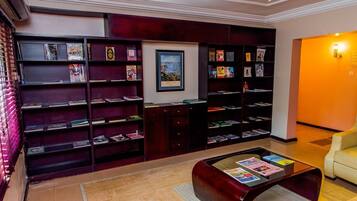 Une bibliothèque avec des étagères, une table basse avec des magazines et un tableau encadré au mur.