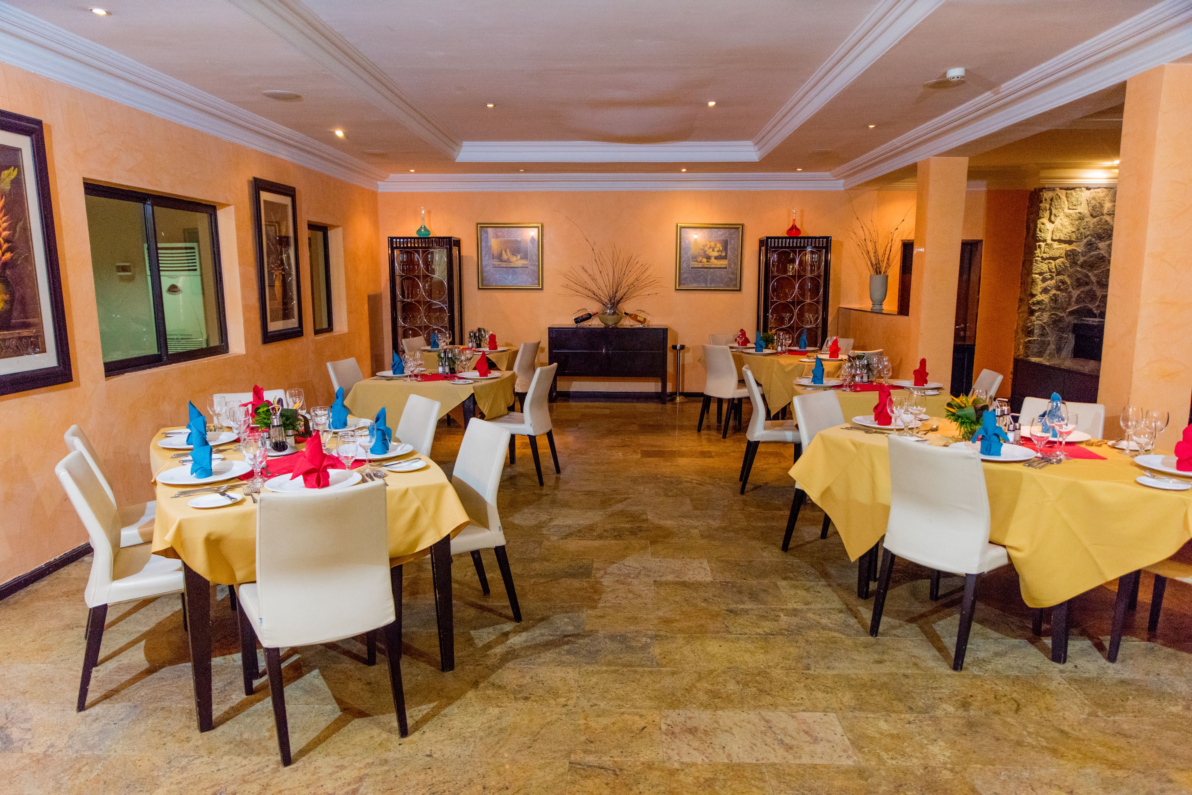 Un comedor con varias mesas dispuestas para los huéspedes, con piso de piedra y obras de arte enmarcadas en las paredes.